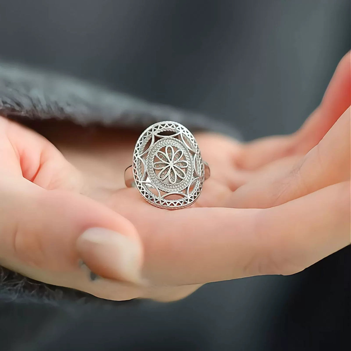 Front view of a silver-tone floral openwork ring worn on a finger