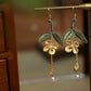 Pair of golden osmanthus leaf tassel earrings on a display rod