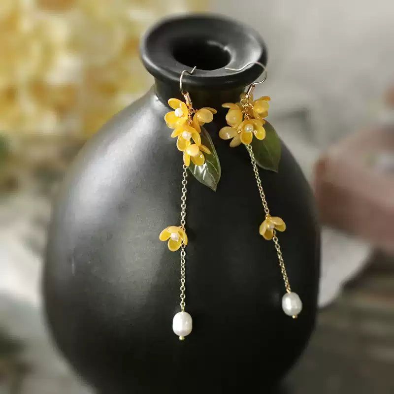 Long golden osmanthus tassel earrings displayed on a dark vase