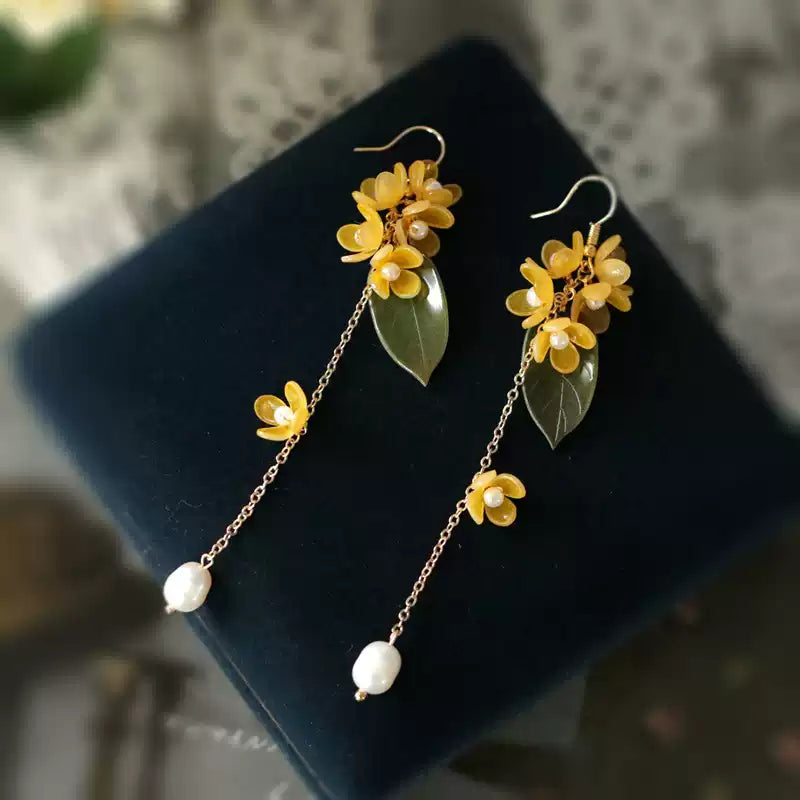 Long golden osmanthus earrings with chain tassels and white bead drops on dark fabric