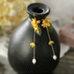 Golden osmanthus flower and leaf tassel earrings hanging on a dark vase