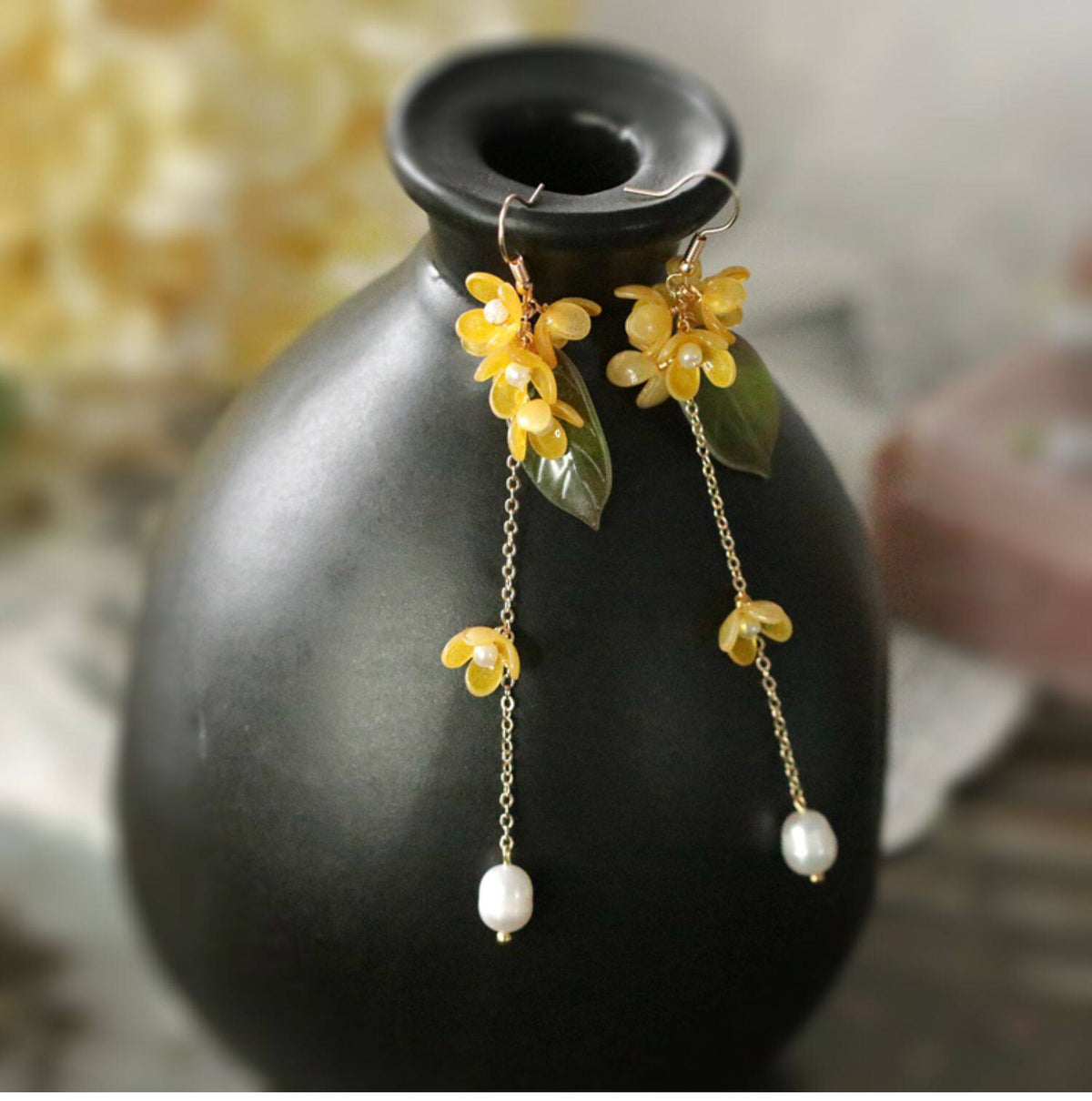 Golden osmanthus flower and leaf tassel earrings hanging on a dark vase
