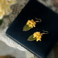 Short gold-tone osmanthus flower and green leaf earrings shown as a pair