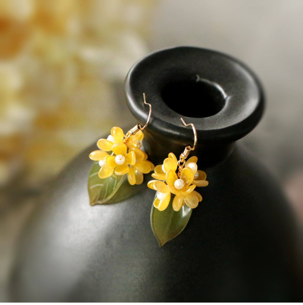 Short osmanthus blossom and leaf earrings displayed against a dark background