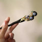 Angled close-up of a dark wood hairpin with peacock feather motifs