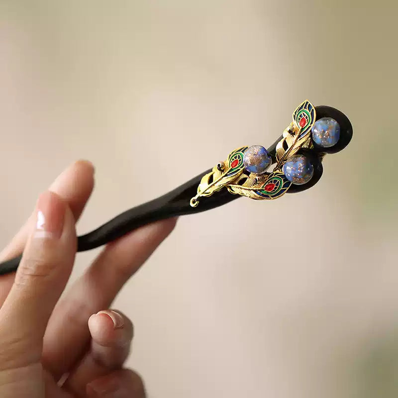 Angled close-up of a dark wood hairpin with peacock feather motifs