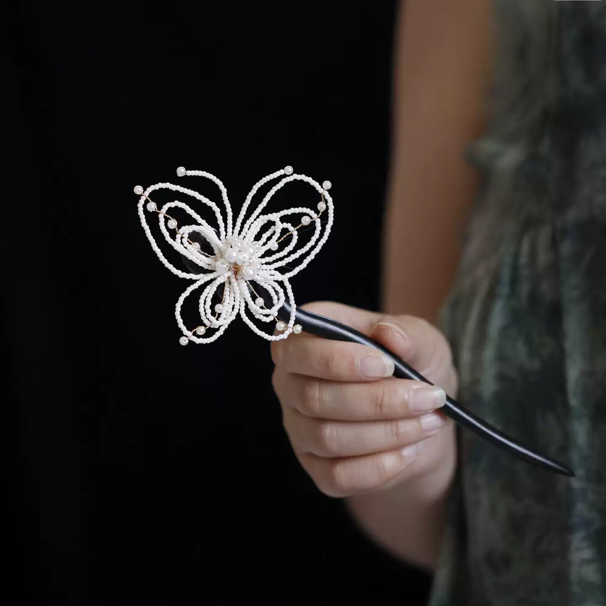 Detailed view of a pearl-style butterfly hairpin held by hand