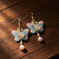 Pink and blue butterfly tassel earrings on a wood surface