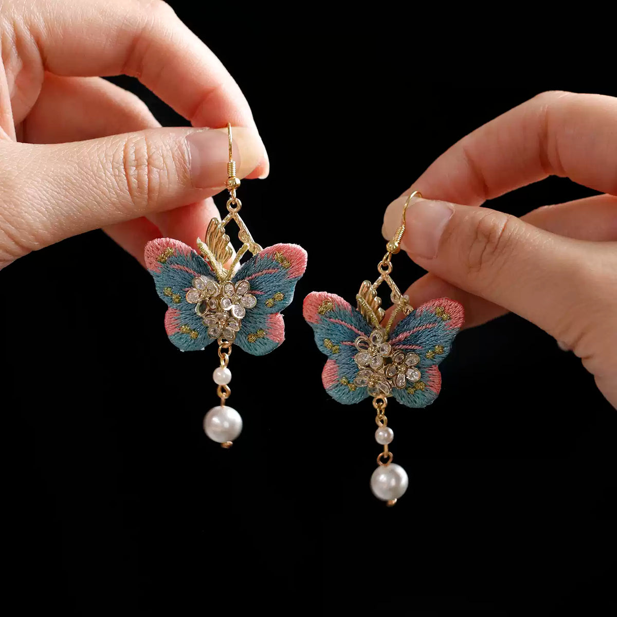 Close-up of embroidered butterfly earrings worn on a hand