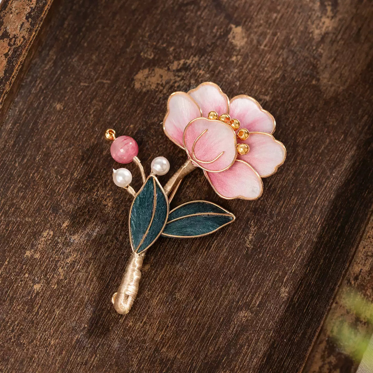 Pink flower brooch with dark green leaves and gold-tone outlines
