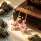 Pink iris flower earrings displayed against a traditional-style wood setting