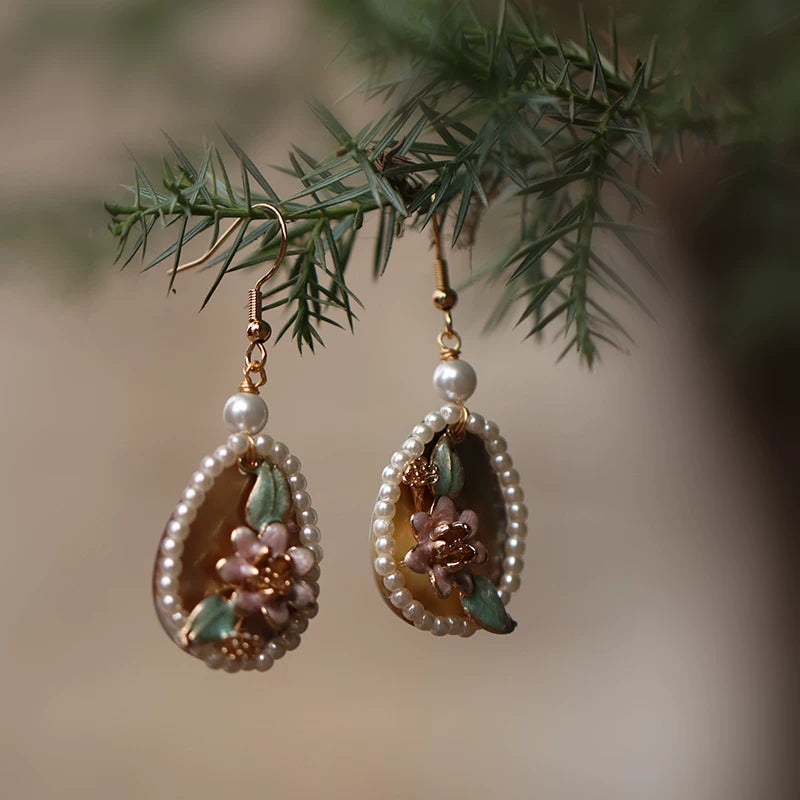 Pair of pink shell flower earrings with faux pearls hanging from a branch