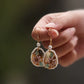 Pair of pink floral drop earrings held by hand, showing the gold-tone hooks