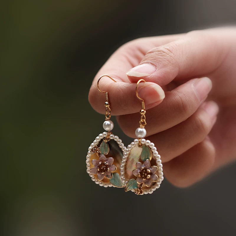Pair of pink floral drop earrings held by hand, showing the gold-tone hooks
