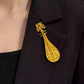 Pipa-shaped copper brooch worn on a dark jacket lapel