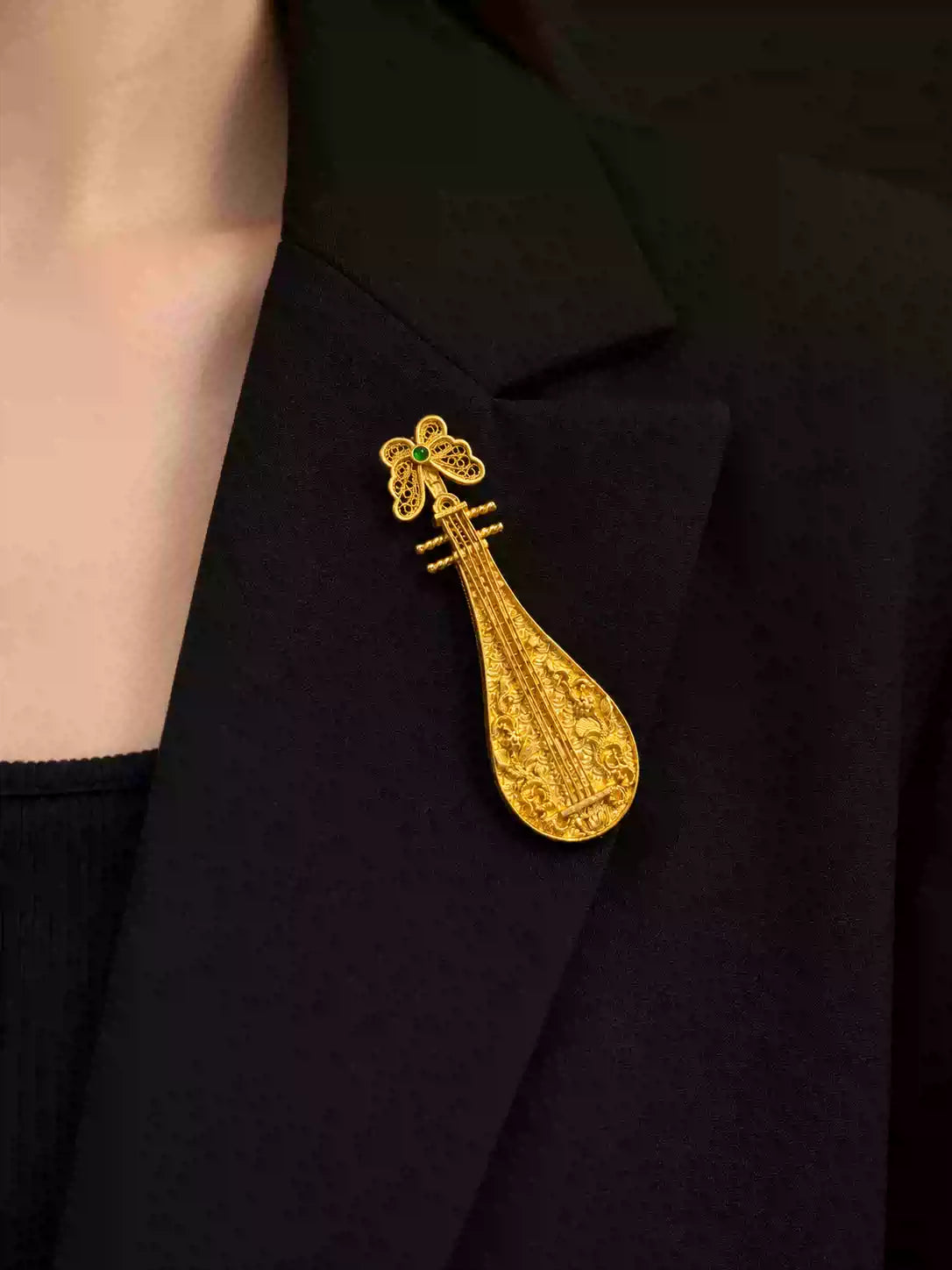 Close view of the gold-tone pipa brooch on a jacket