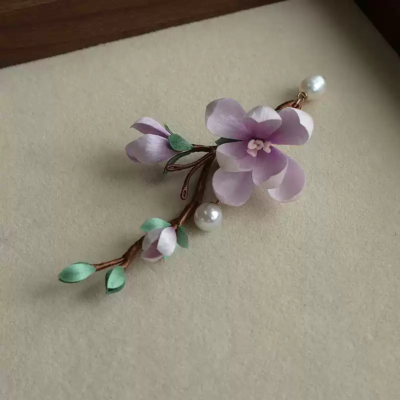 Angled view of the floral brooch with a large bloom, smaller buds, and leafy branch