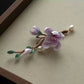 Close-up of the purple floral branch brooch showing layered petals and bead accents
