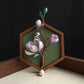 Purple floral branch brooch with green leaves and white bead accents displayed on a stand