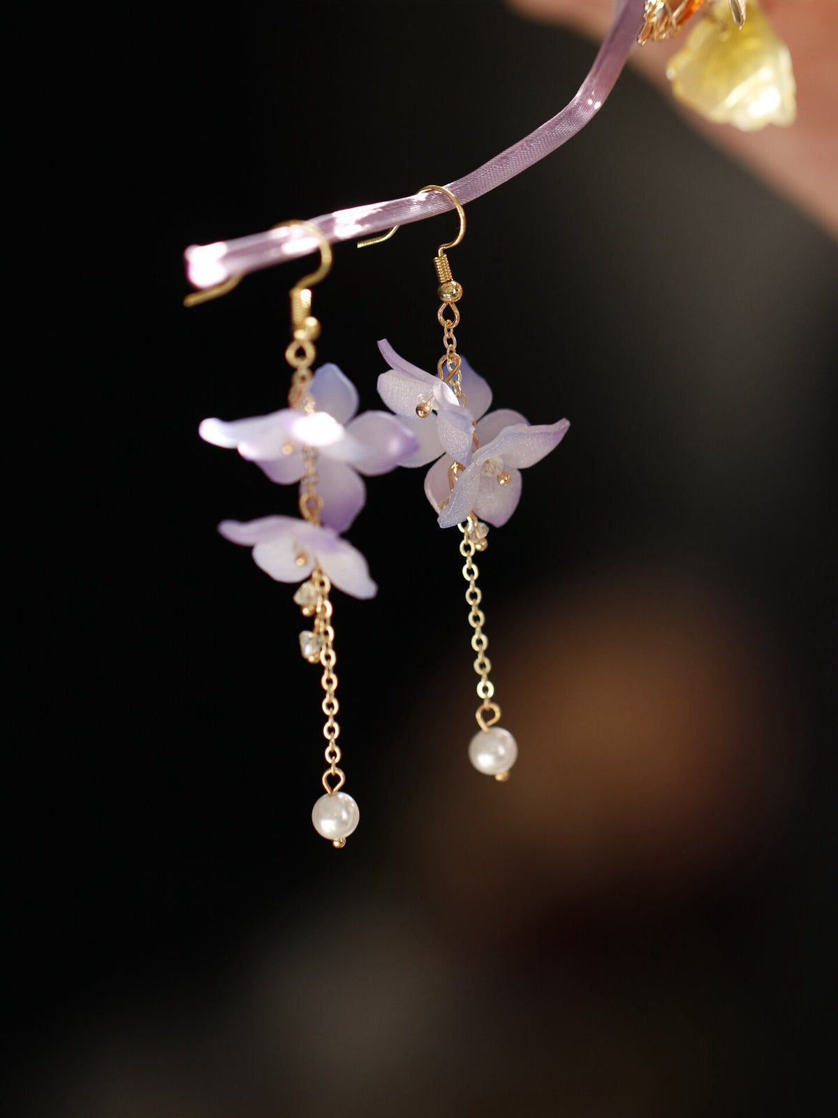 Pair of long purple flower earrings worn, side view