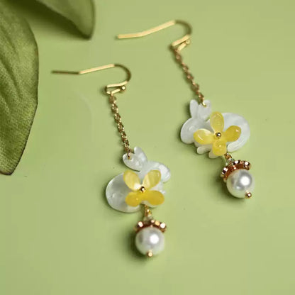 Pair of rabbit and yellow flower drop earrings on a soft green background