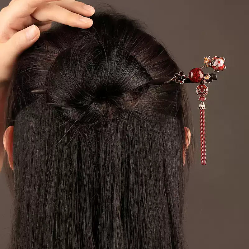 Red tassel hairpin worn in a dark bun, rear view