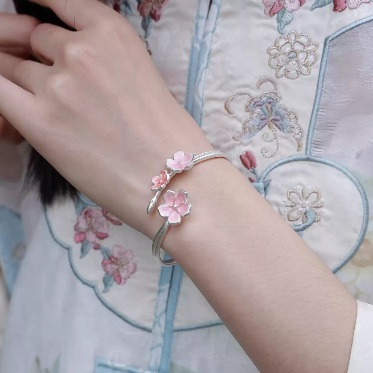 Adjustable silver cuff bracelet with pink cherry blossom details worn with embroidered clothing