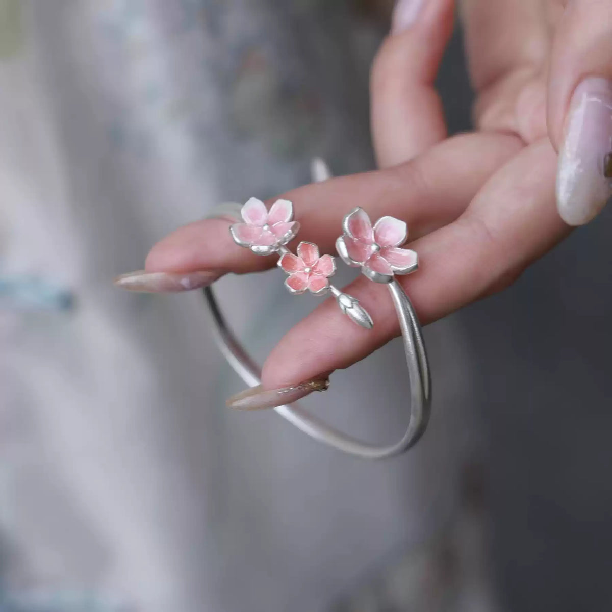 Close-up of pink enamel cherry blossom ornaments on an open silver cuff bracelet
