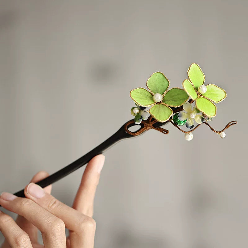 Close-up of a dark wooden hair stick with green silk flowers and pearl accents