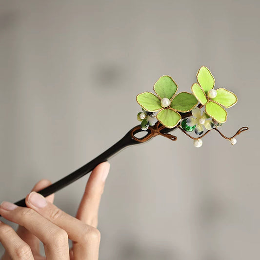Close-up of a dark wooden hair stick with green silk flowers and pearl accents
