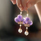 Close-up detail of violet floral earrings and white bead drops