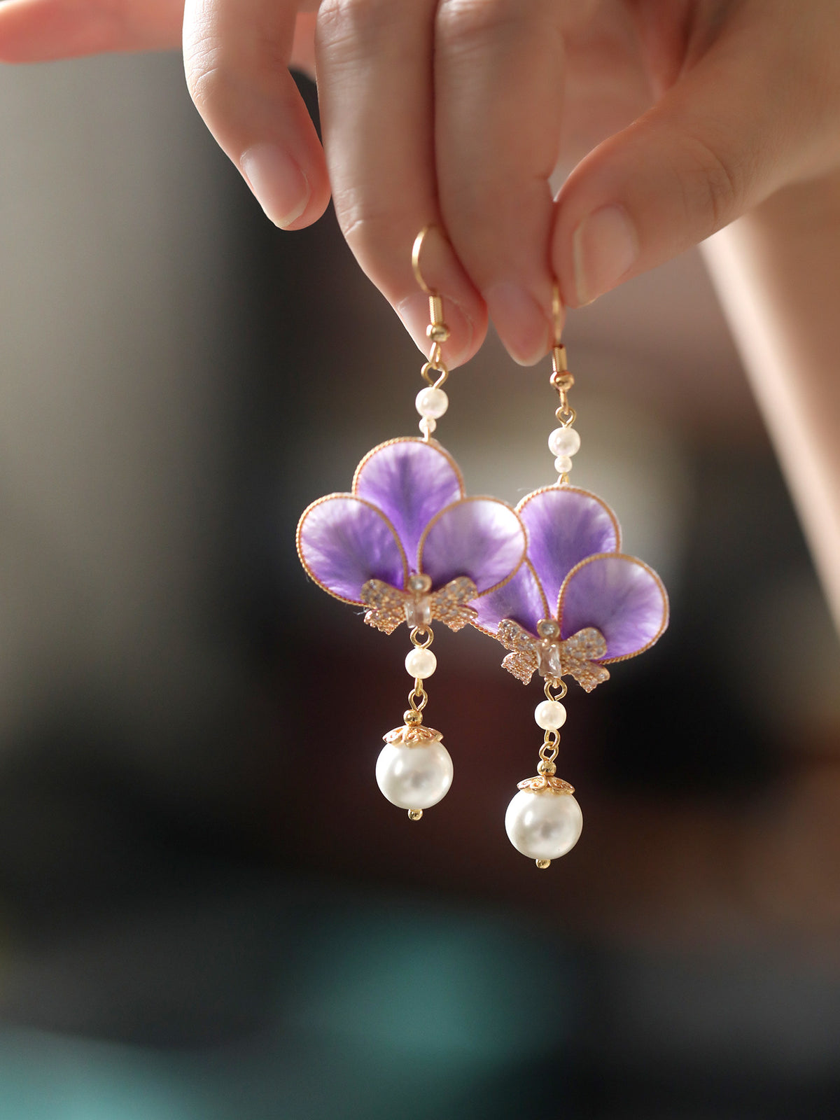 Close-up detail of violet floral earrings and white bead drops