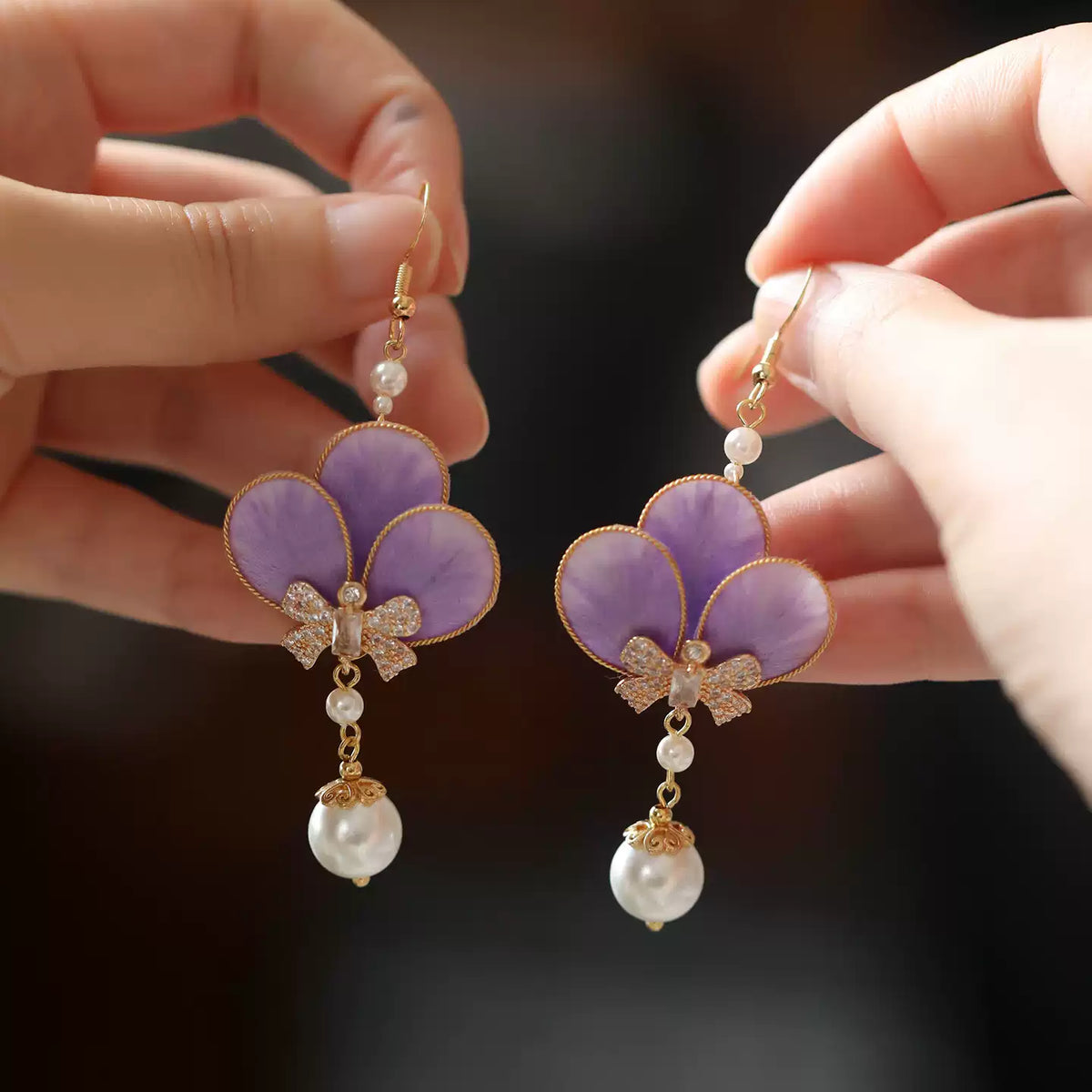 Pair of violet flower drop earrings held for a closer view