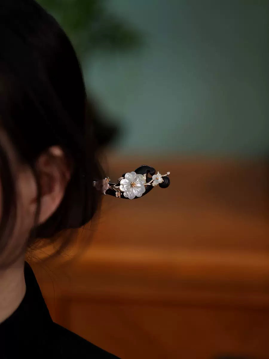 White shell flower on a dark ebony wood hair stick, shown in a bun