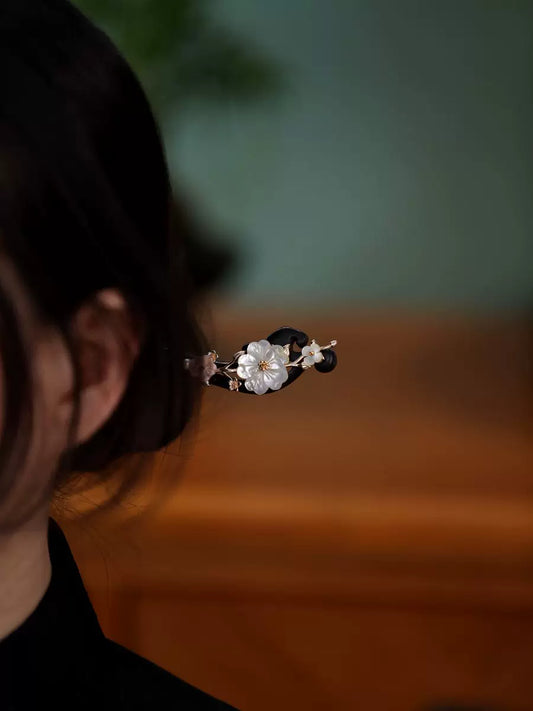 White shell flower on a dark ebony wood hair stick, shown in a bun