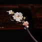 Close-up of white mother-of-pearl flower and pink floral details on a dark wooden hair stick