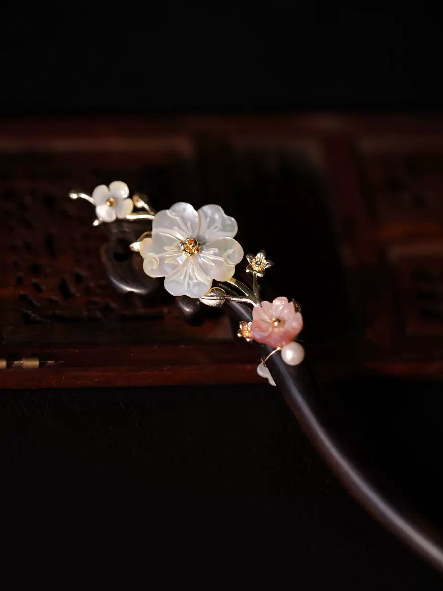 Close-up of white mother-of-pearl flower and pink floral details on a dark wooden hair stick