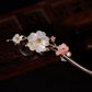 White shell floral ornament and gold-tone branches on a dark wood hair stick