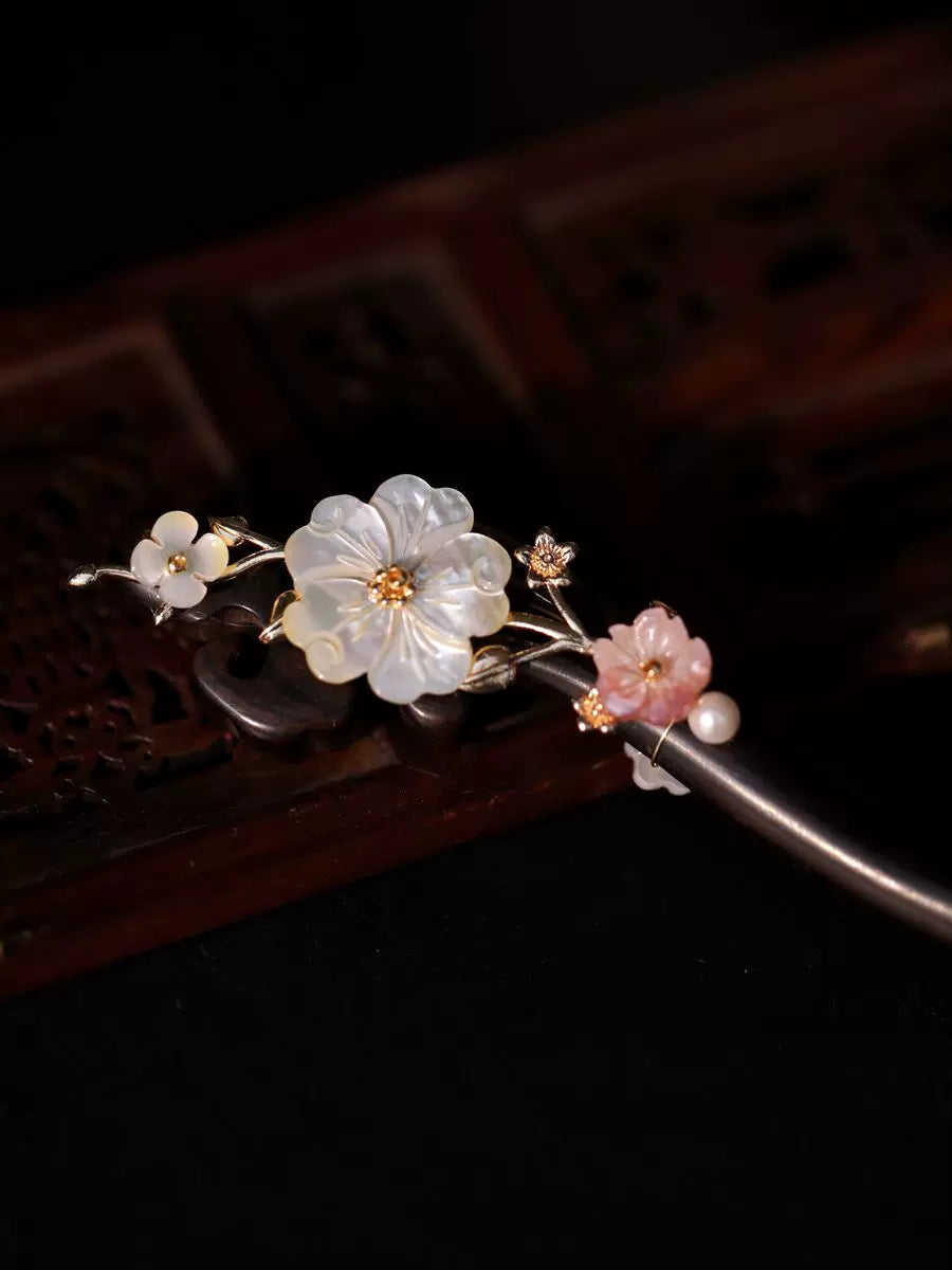 White shell floral ornament and gold-tone branches on a dark wood hair stick